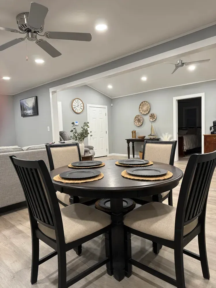 Modern dining room with a round black table, beige chairs, and ceiling fans under recessed lights