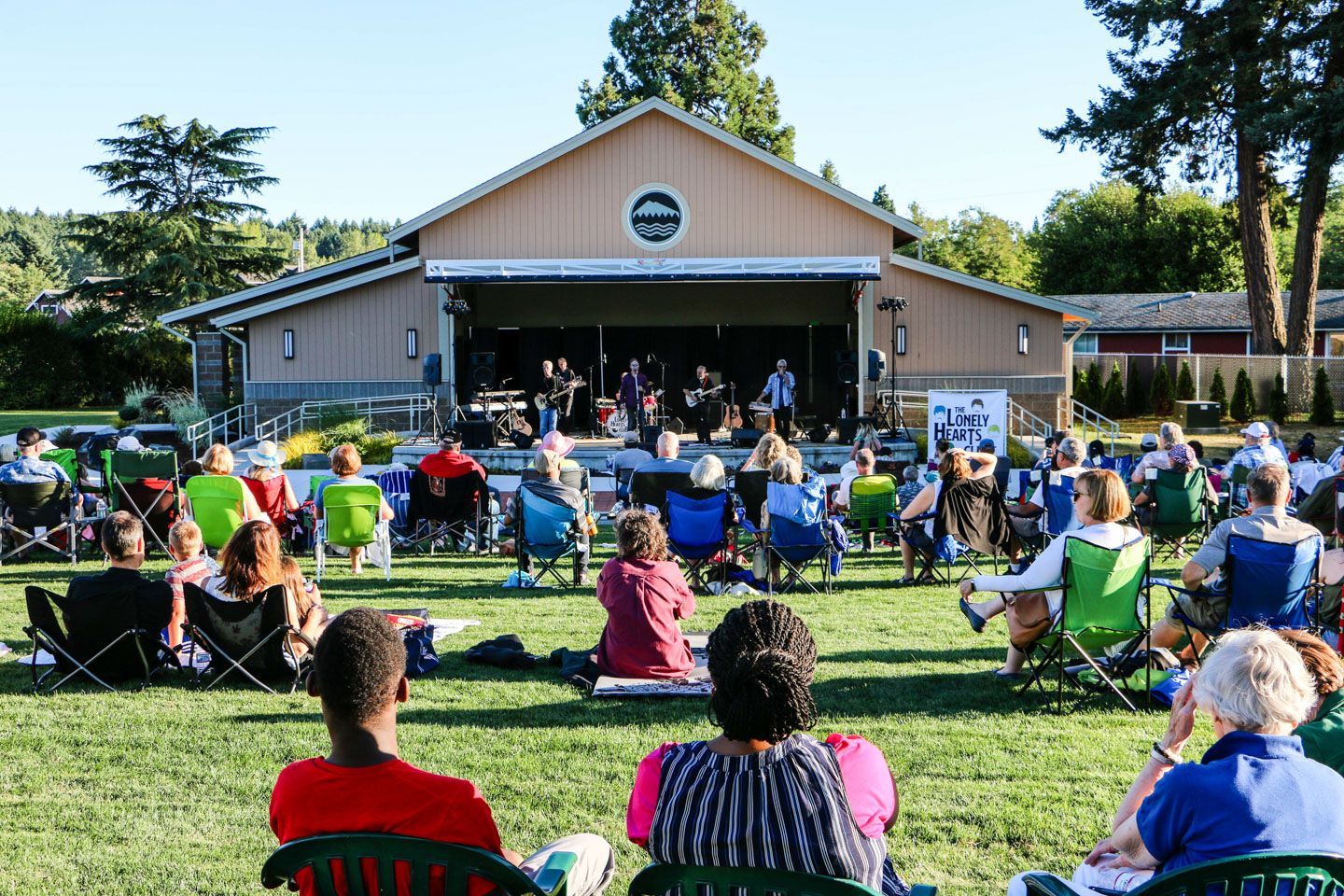 Outdoor concert audience seated on grass facing a pavilion stage in a park