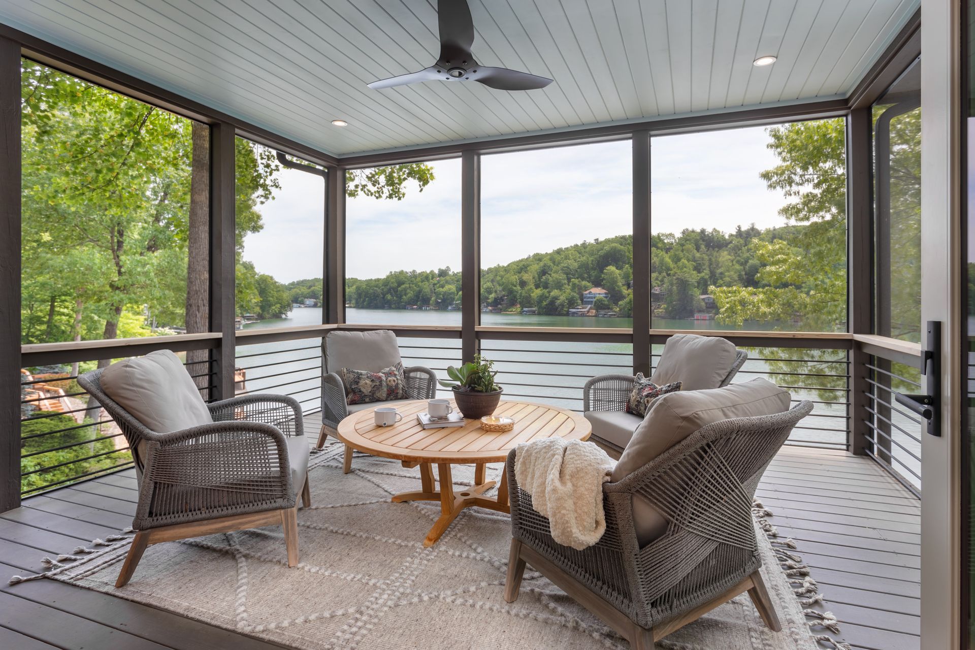 Covered lakeside porch with wicker chairs, round table, and a view of trees and water