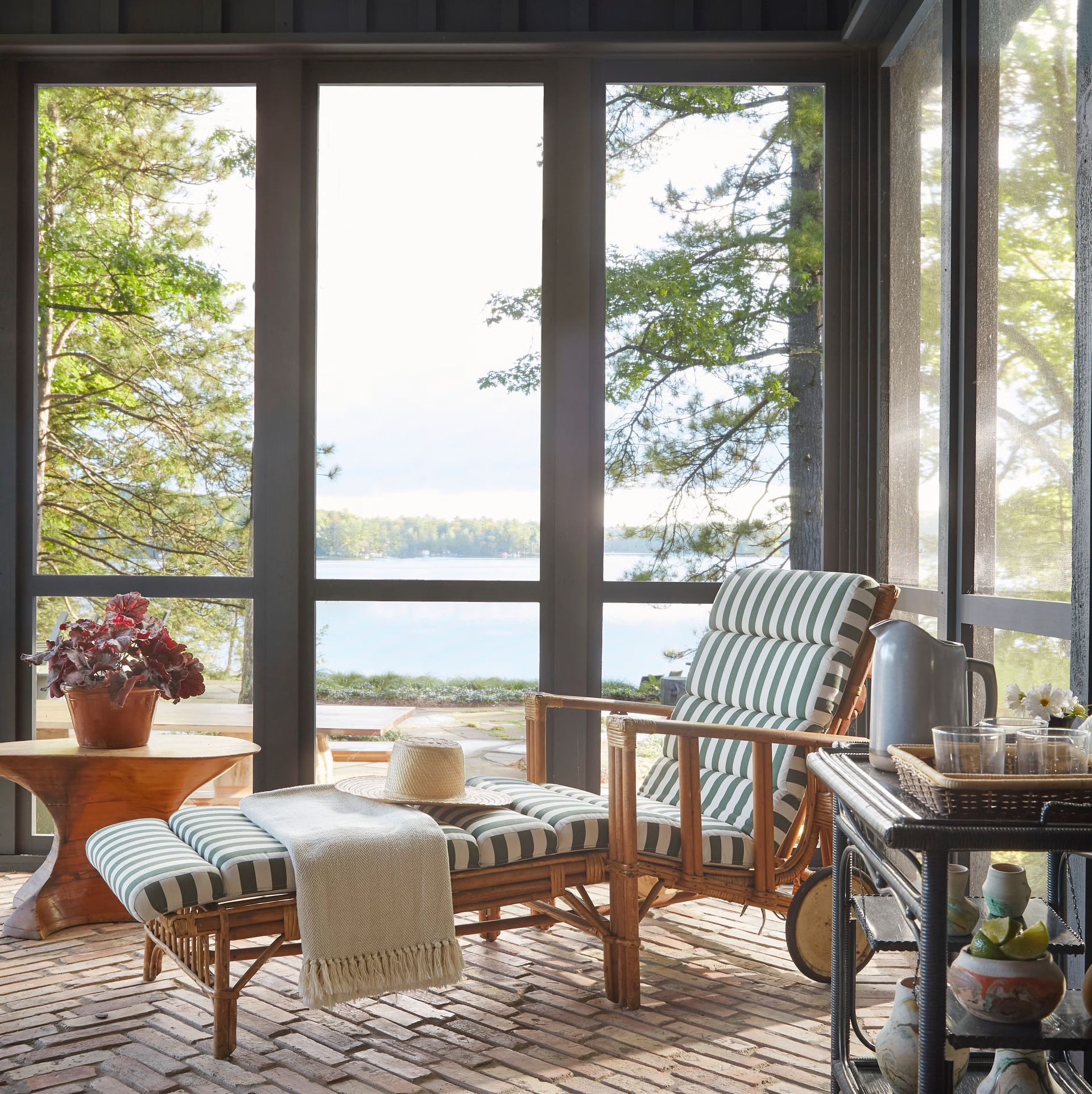 Cozy sunroom with wicker chair, striped cushion, ottoman, and lake view through large windows