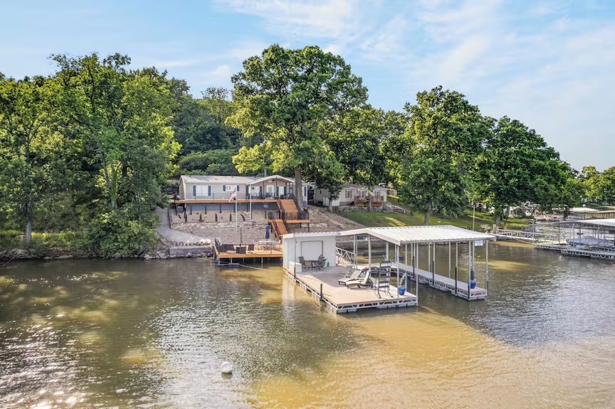 Riverfront dock with boats, a covered slip, and a house nestled among trees on a calm shoreline