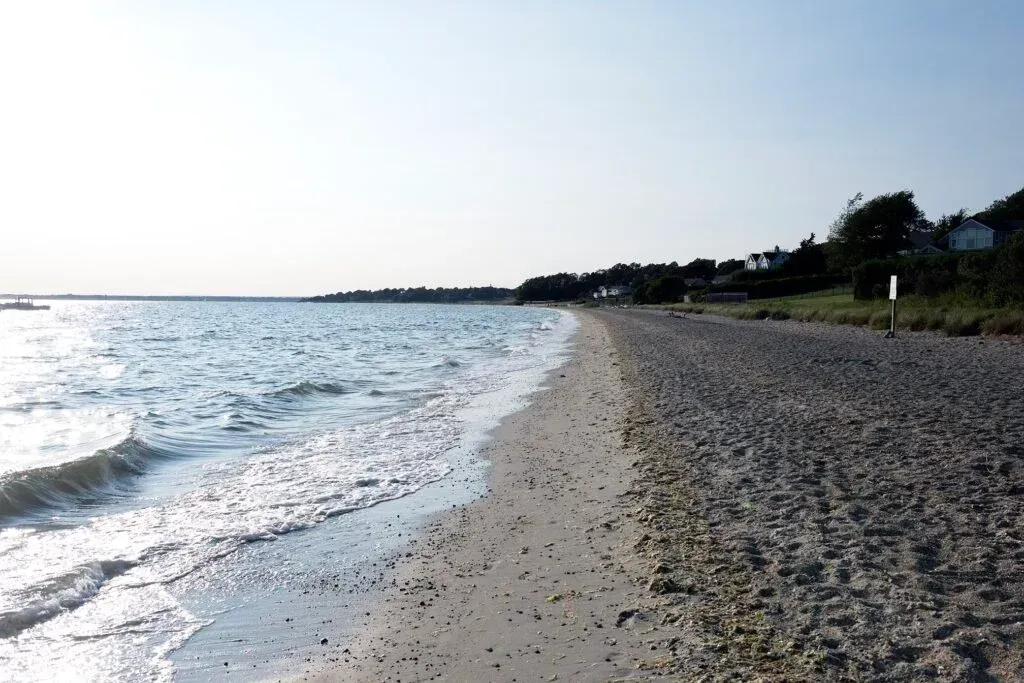 Rocky beach with gentle waves and a bright, hazy shoreline stretching into the distance