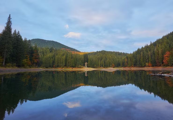 Calm forest lake reflecting pine-covered hills and a pastel sunset sky