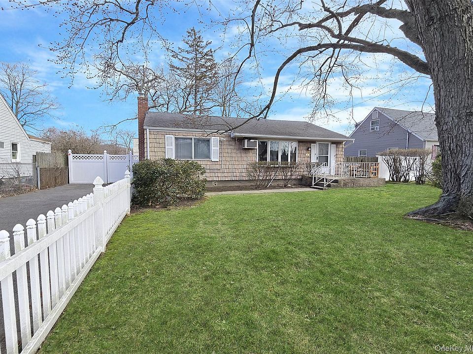 Suburban house with white fence and large green lawn under a clear blue sky