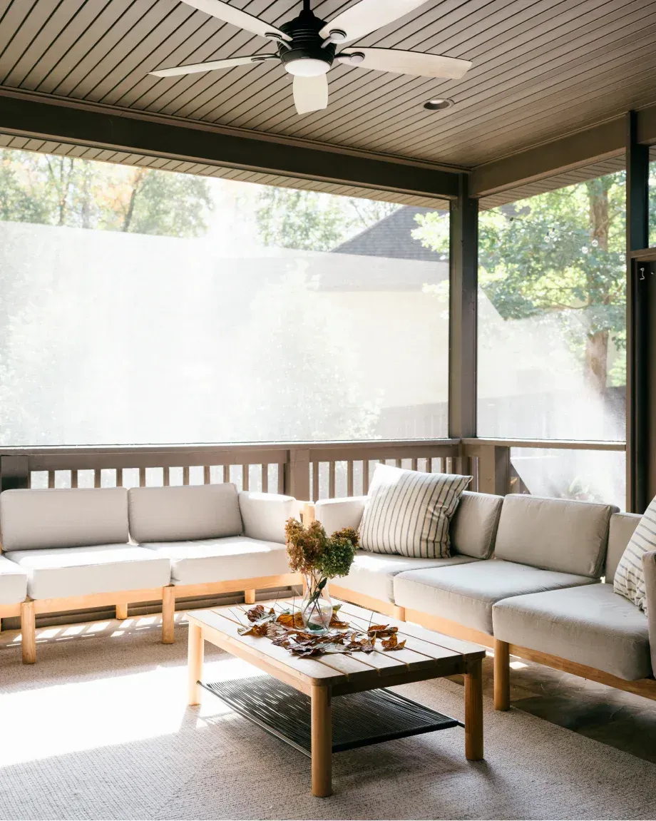 Covered porch with white sectional sofa, coffee table, and ceiling fan in a bright, airy outdoor living space