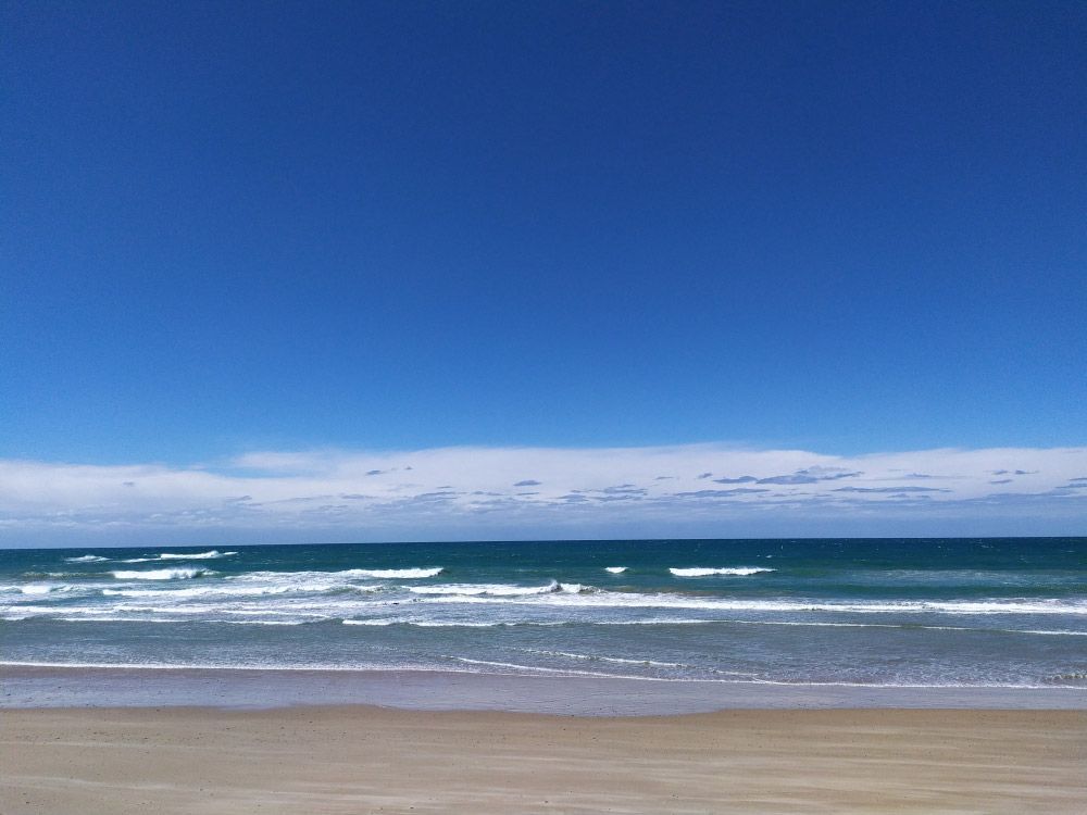 A Beach With A Blue Sky And Waves Coming In — Mid Coast Flooring & Blinds In Old Bar, NSW