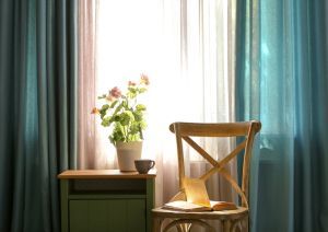 A Chair With A Book On It Is Sitting In Front Of A Window — Mid Coast Flooring & Blinds In Taree, NSW