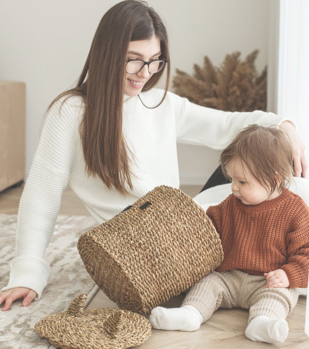 Woman and toddler sitting on a rug with a wicker basket in a bright room