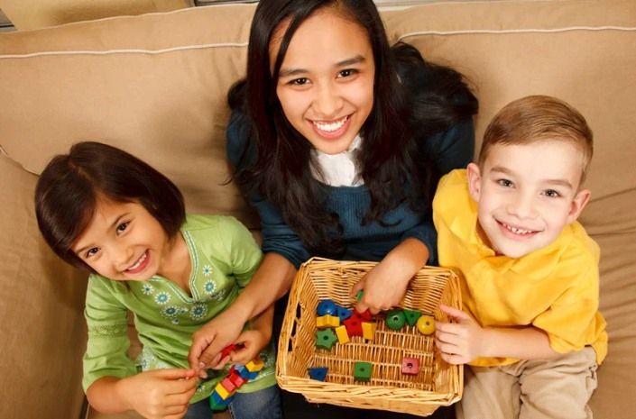 Three children smiling on a couch with a toy basket and colorful blocks