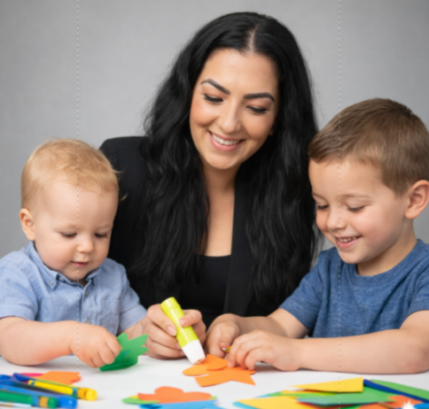 Three children and an adult smiling while making colorful paper crafts at a table