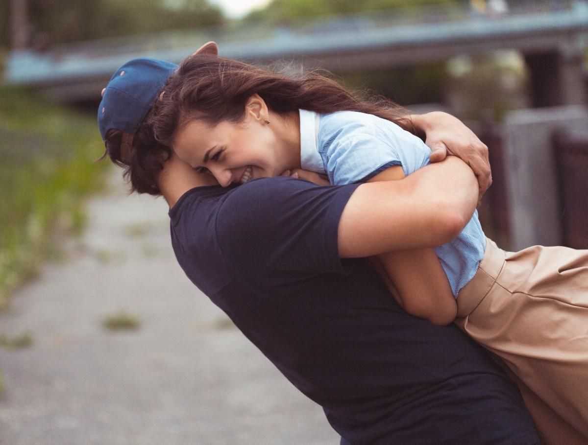 Man lifting and hugging woman while both laughing representing attraction, confidence, and strong romantic connection