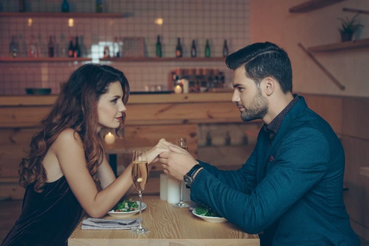 couple holding hands across dinner table building emotional connection while dating