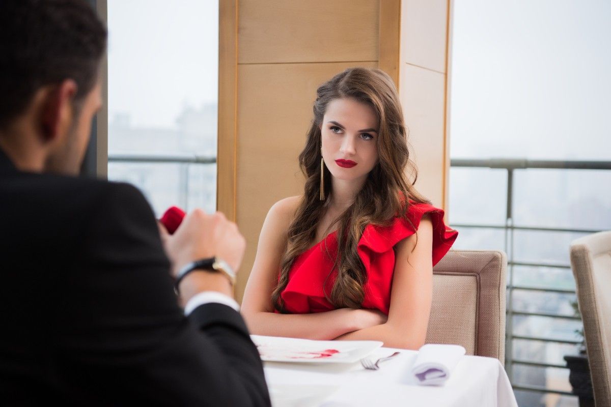 Woman looking annoyed at dinner while man presents engagement ring box during luxury matchmaking date in Texas