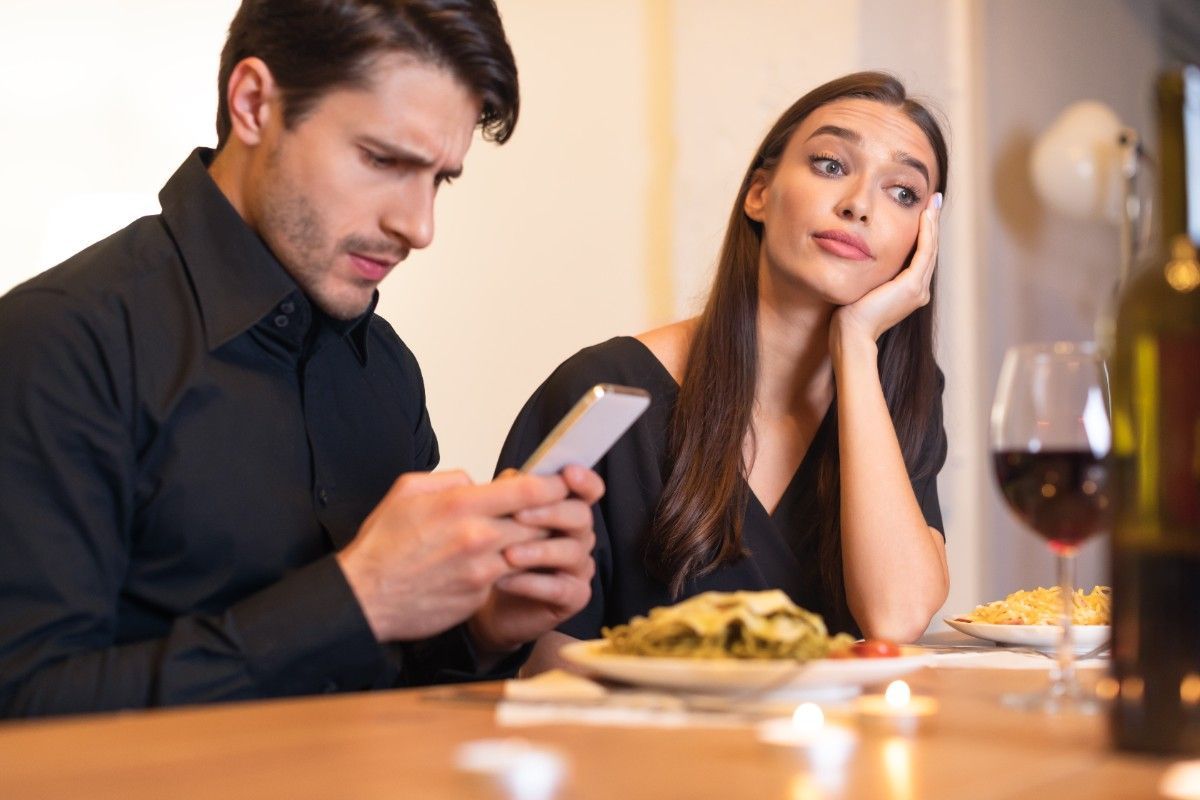 woman feeling frustrated while man distracted on phone during date