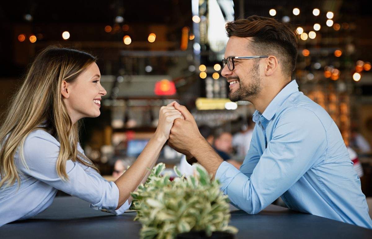 Man and woman holding hands and smiling across table representing successful matchmaking and relationship guidance
