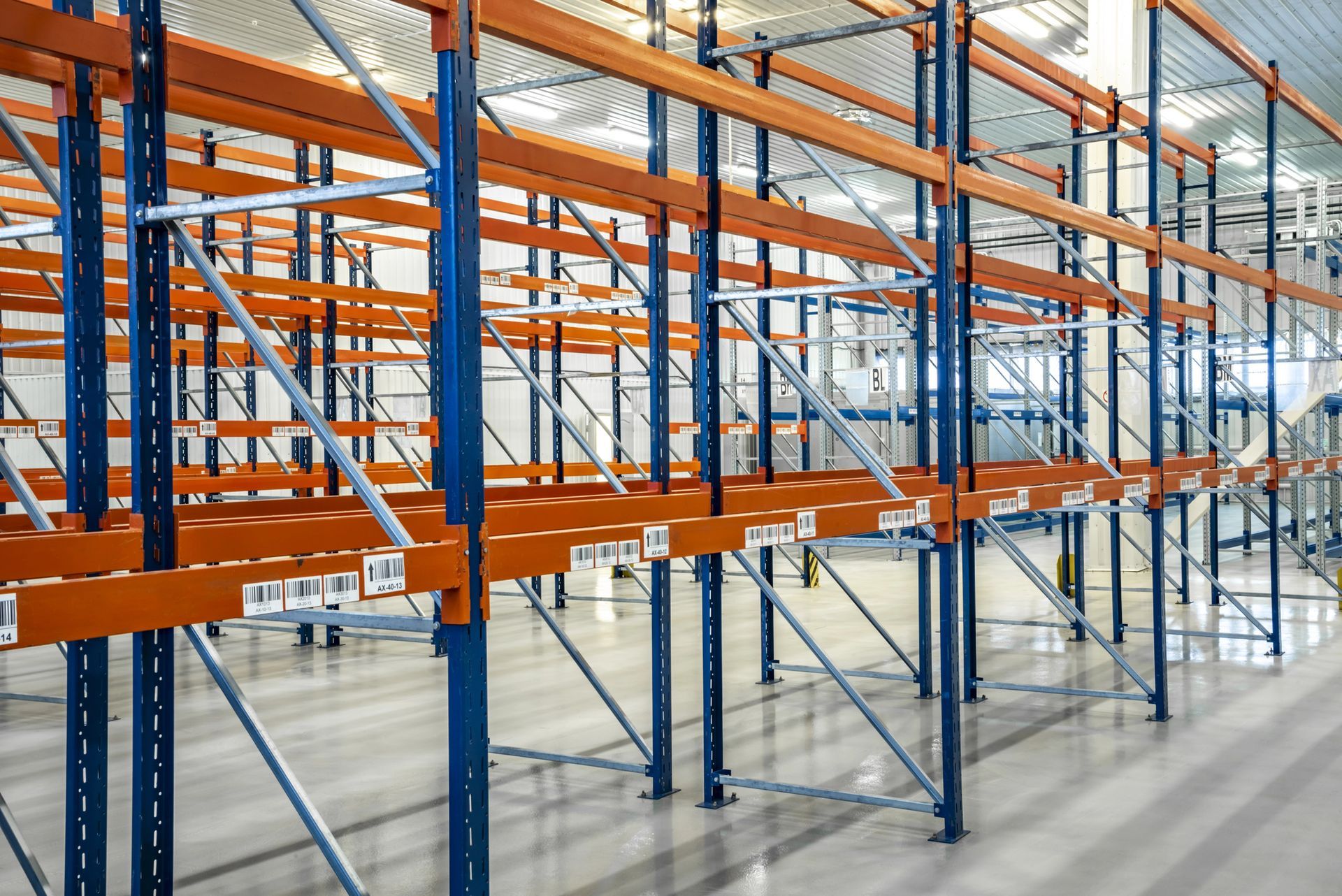 Magazzino vuoto con alte scaffalature blu e arancioni e pavimenti in cemento.