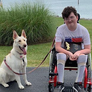 A boy in a wheelchair is sitting next to a white dog on a leash.