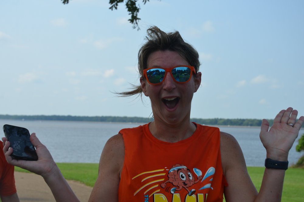 A man wearing sunglasses and an orange tank top is holding a cell phone.