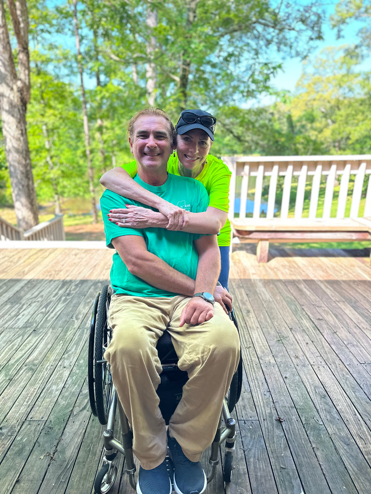 A man in a wheelchair is being hugged by a woman on a deck.
