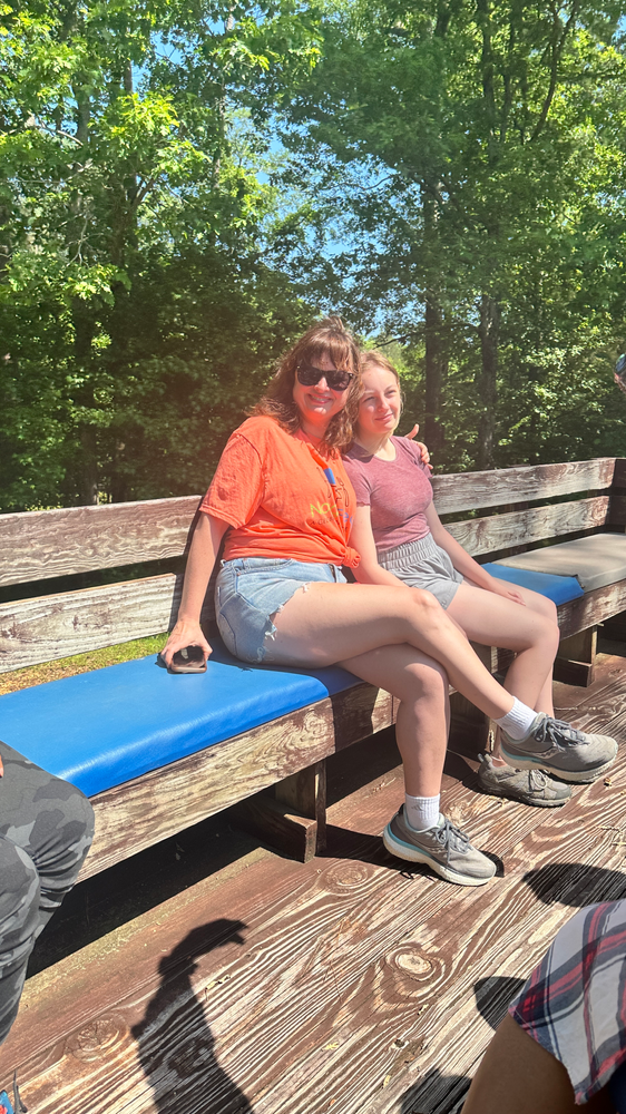 Two women are sitting on a wooden bench with their legs crossed.