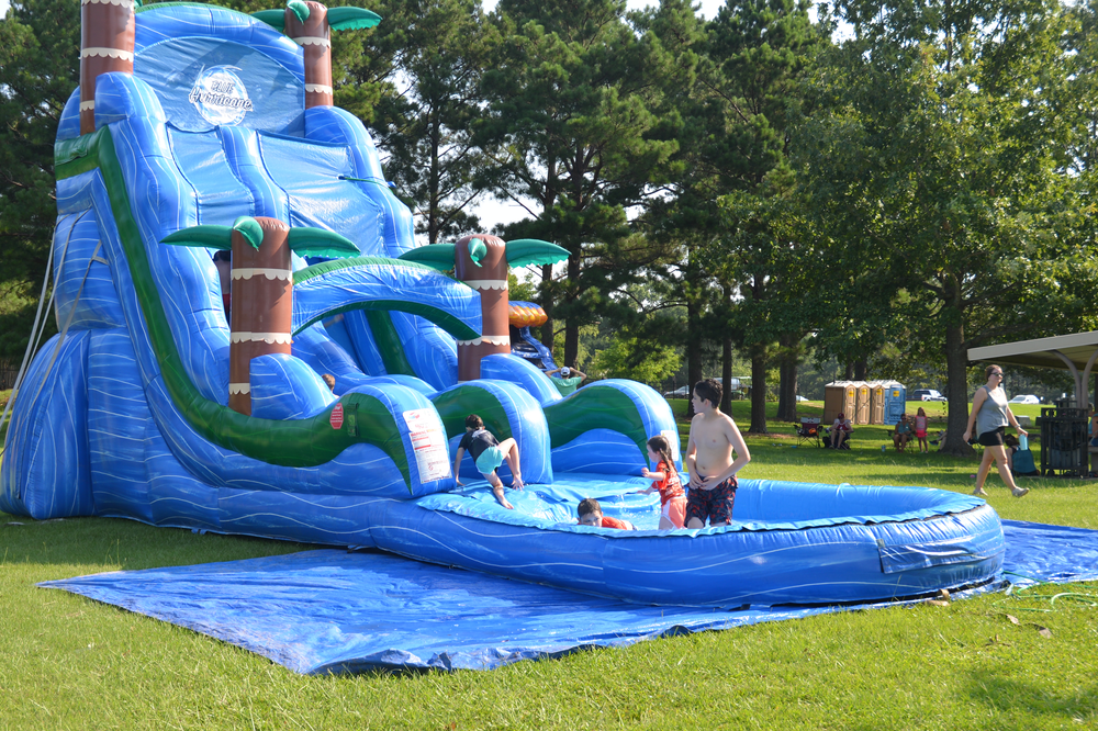 A group of children are playing in an inflatable water slide in a park.