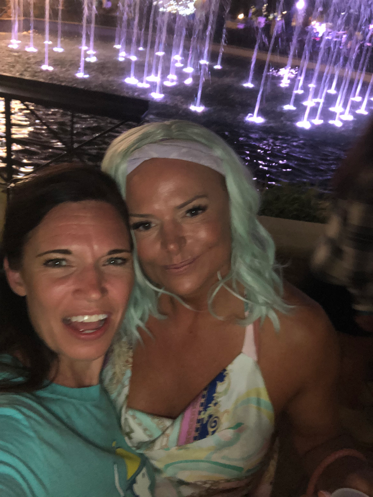 Two women are posing for a picture in front of a fountain.