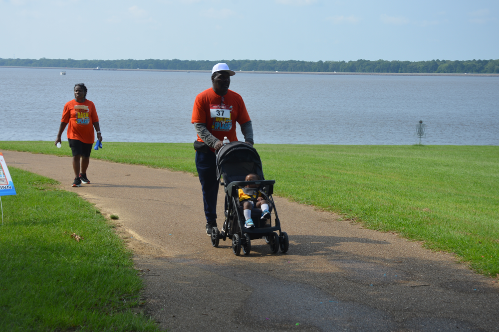 A man is pushing a stroller down a path next to a body of water.