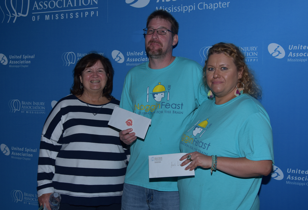 A man and two women are standing next to each other holding a check.