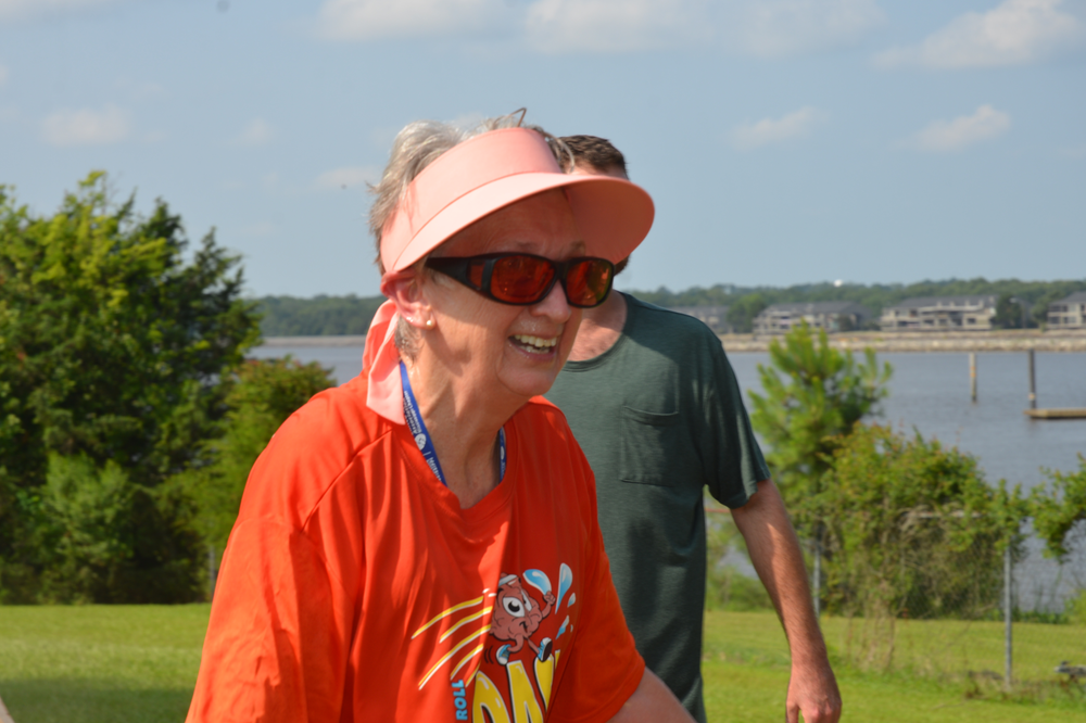 A woman wearing an orange shirt and a pink visor is smiling.