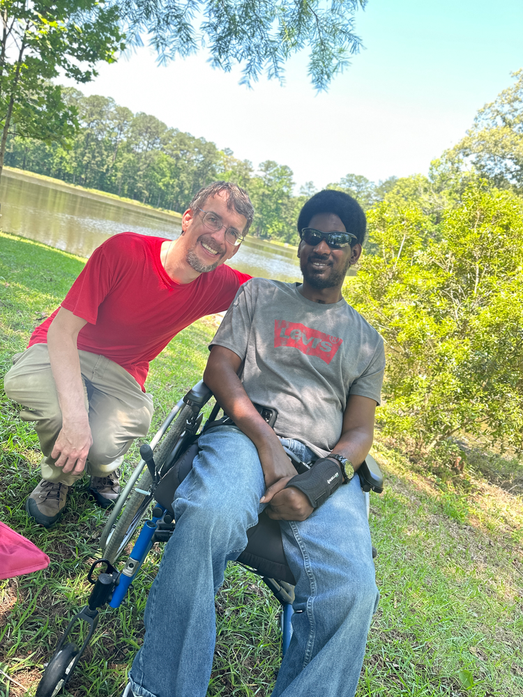 A man in a wheelchair is sitting next to a man in a red shirt.