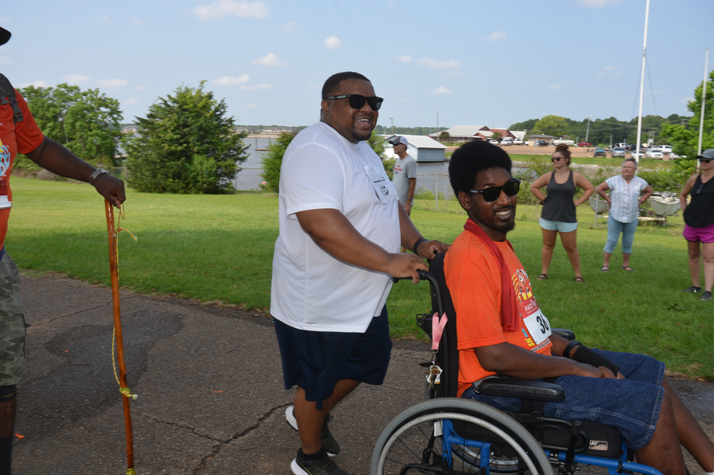A man in a wheelchair is being pushed by a man with a cane.