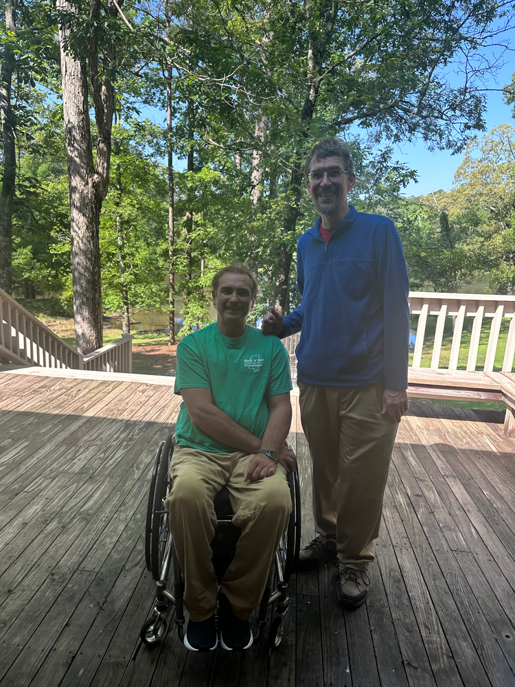 A man in a wheelchair is standing next to another man on a deck.