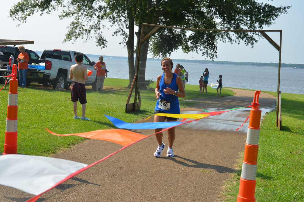 A woman in a blue tank top is crossing the finish line of a race