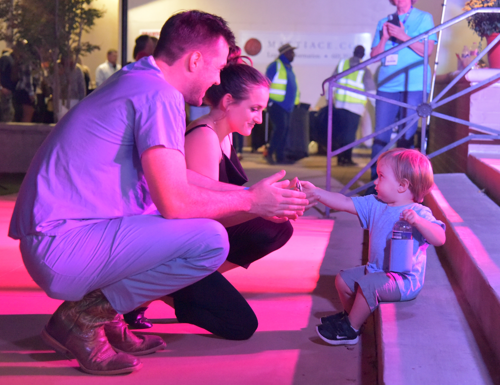 A man and woman are kneeling down next to a little boy sitting on a set of stairs.
