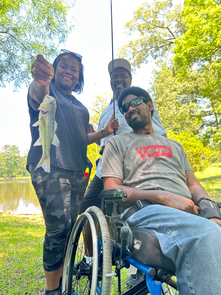 A man in a wheelchair is fishing with a woman holding a fish.