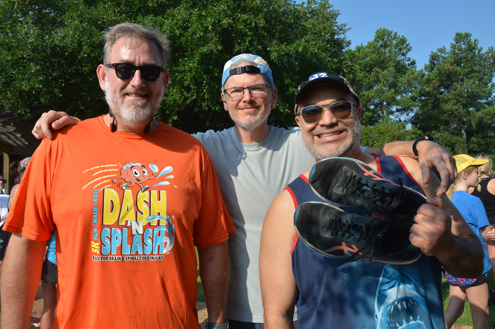 Three men are posing for a picture and one of them is wearing an orange shirt that says dash splashed