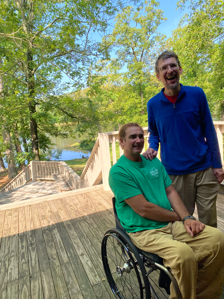 A man in a wheelchair is standing next to another man on a deck.