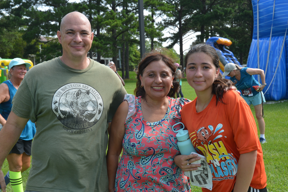 A man , a woman and a girl are posing for a picture in a park.