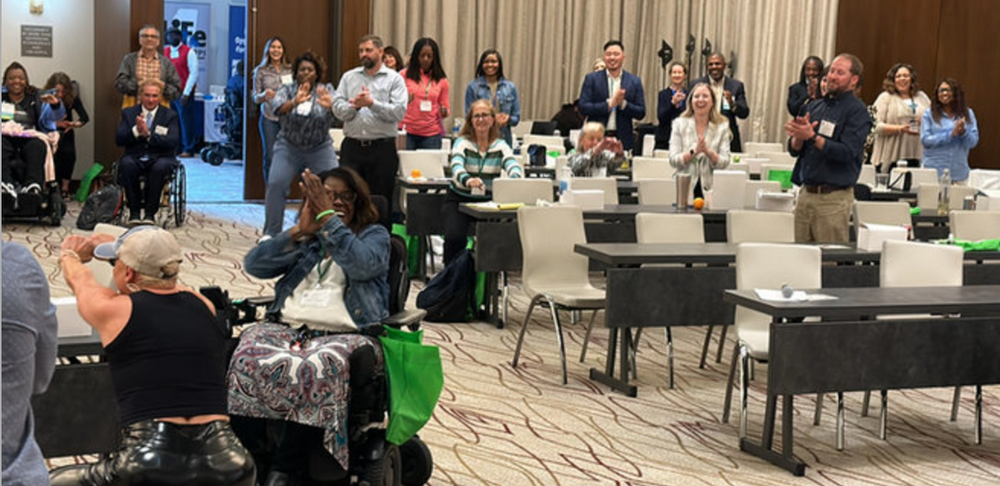 A group of people are standing in a room with tables and chairs.