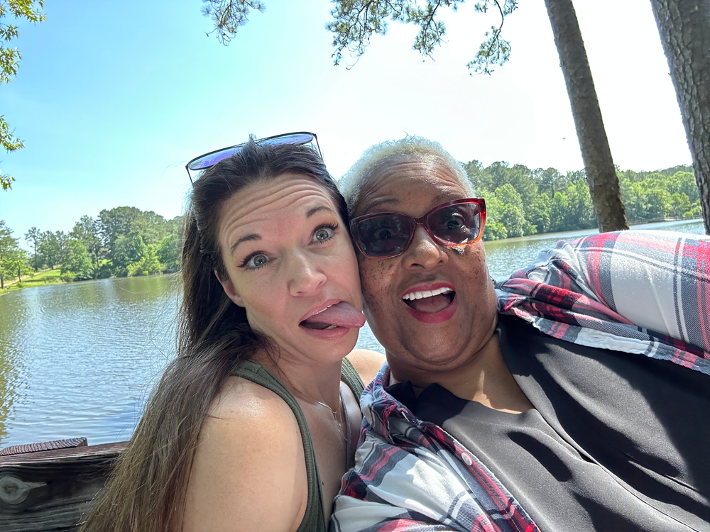 Two women are posing for a picture in front of a lake.
