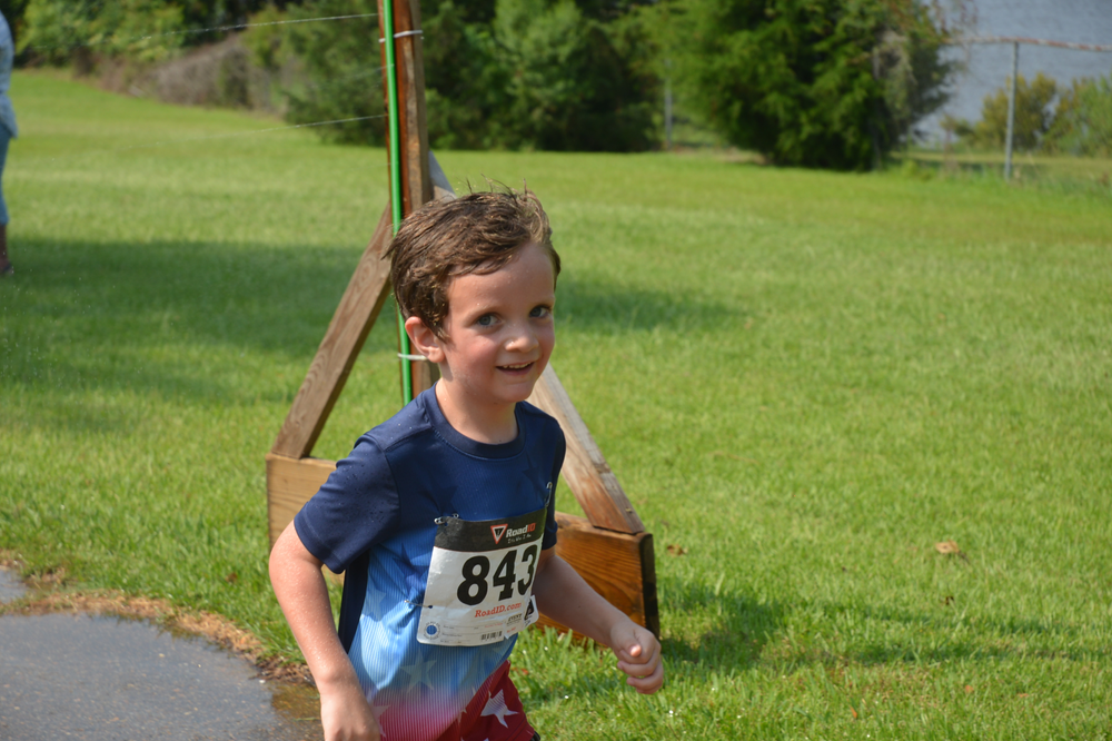 A young boy is running in a field with a number on his shirt.