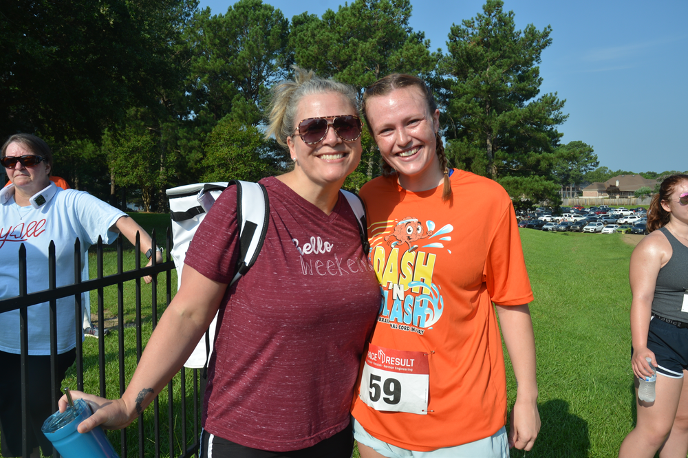 Two women are posing for a picture in a park . one of the women is wearing an orange shirt with the number 59 on it.