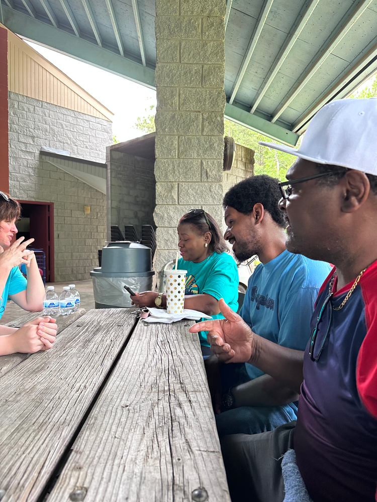 A group of people are sitting at a wooden picnic table.
