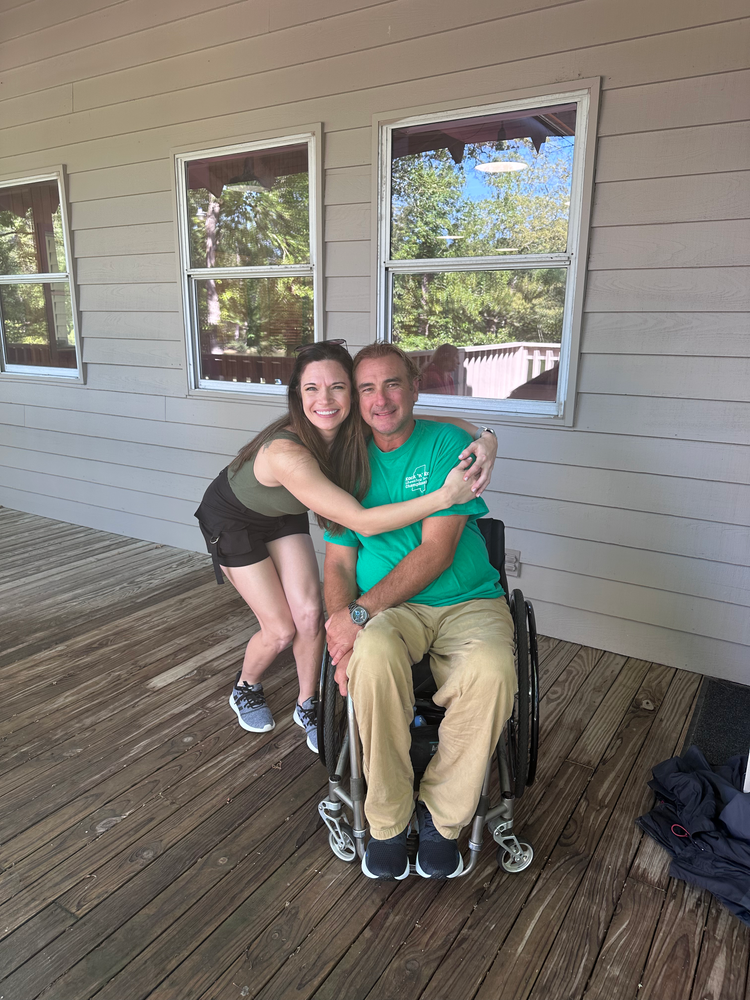 A woman is hugging a man in a wheelchair on a porch.