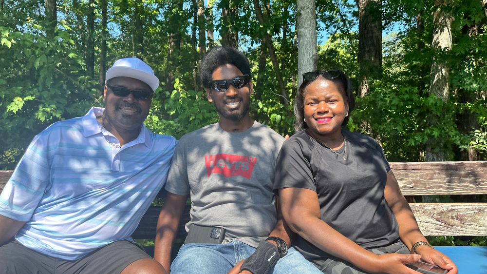 A man and two women are sitting on a wooden bench.