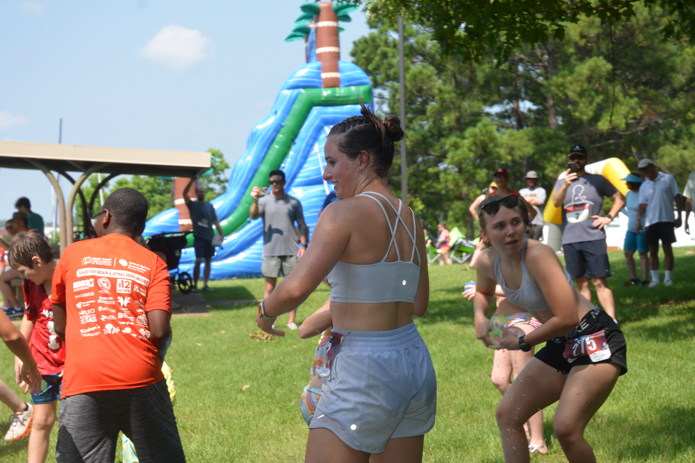 A group of people are dancing in a park in front of a water slide.