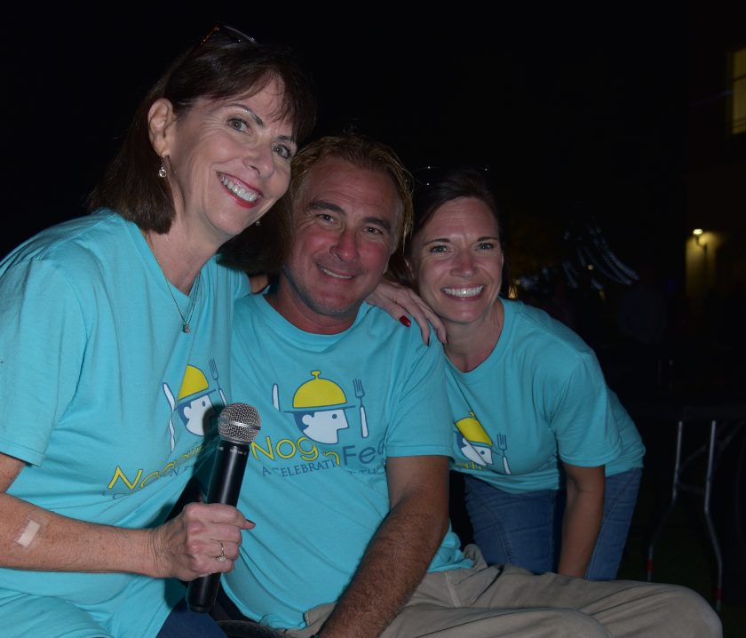 A man and two women are posing for a picture and the man is holding a microphone