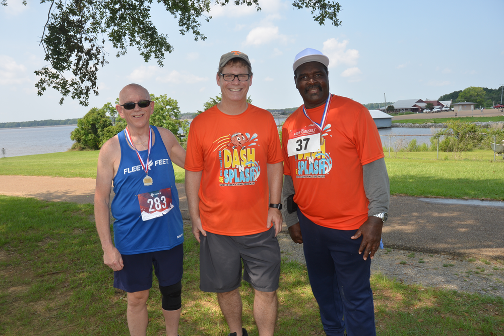 Three men wearing orange shirts are posing for a picture in a park.
