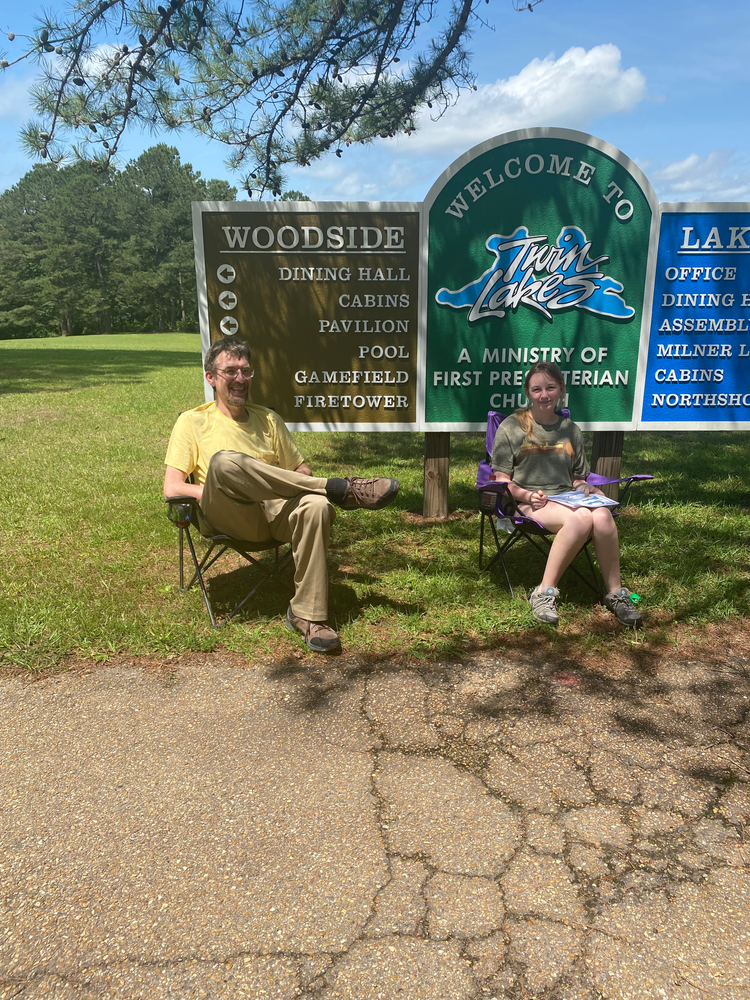A man and a woman are sitting in chairs in front of a welcome to woodside sign.