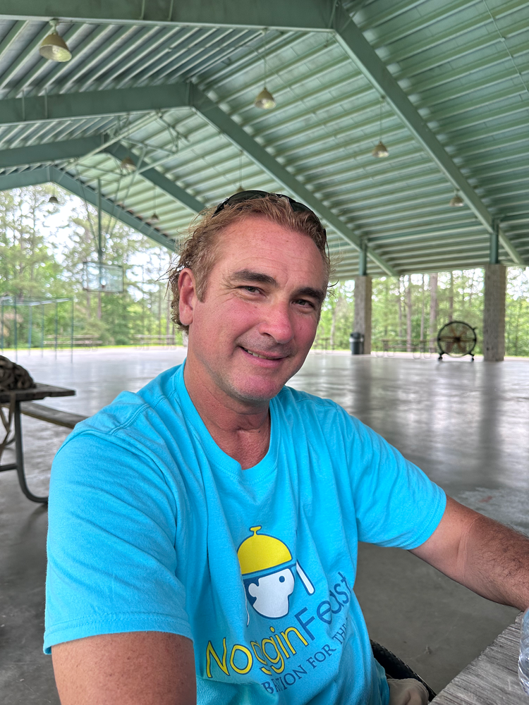 A man in a blue shirt is sitting at a table in a pavilion.